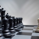White pawn against the background of dark chess pieces