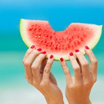 Hand holding slice of watermelon on the beach.